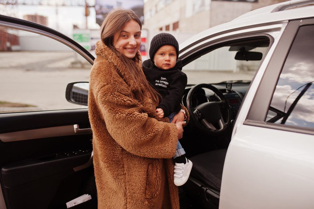mladá žena s malým dieťatkom na rukách pózuje pred novým autom
